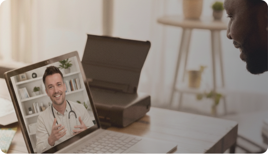 Person having a video consultation with a doctor on a laptop showing a smiling male doctor in a white coat.