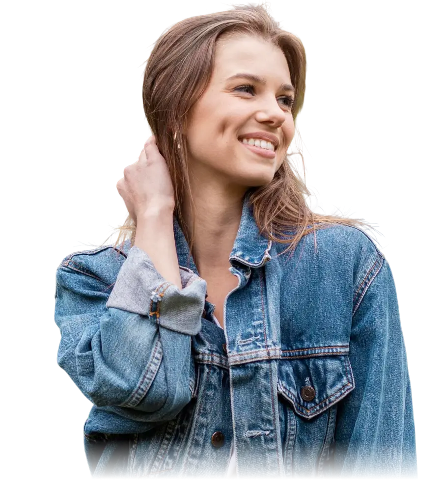 Smiling woman with long light brown hair wearing a rolled-up denim jacket and touching her hair.
