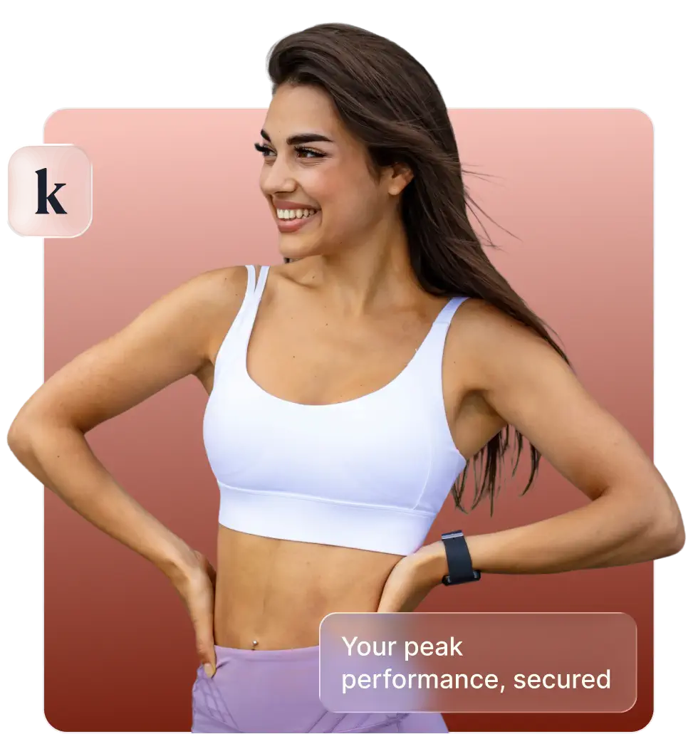 Smiling woman in white sports bra and purple leggings with hands on hips, wearing a fitness tracker.