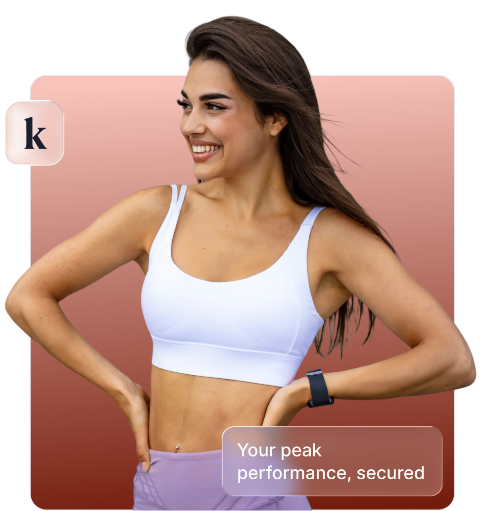 Smiling woman in white sports bra and purple leggings with hands on hips, wearing a fitness tracker.