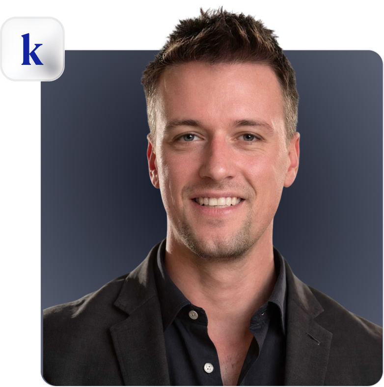 Smiling man with short brown hair wearing a dark blazer and black shirt against a dark gradient background.