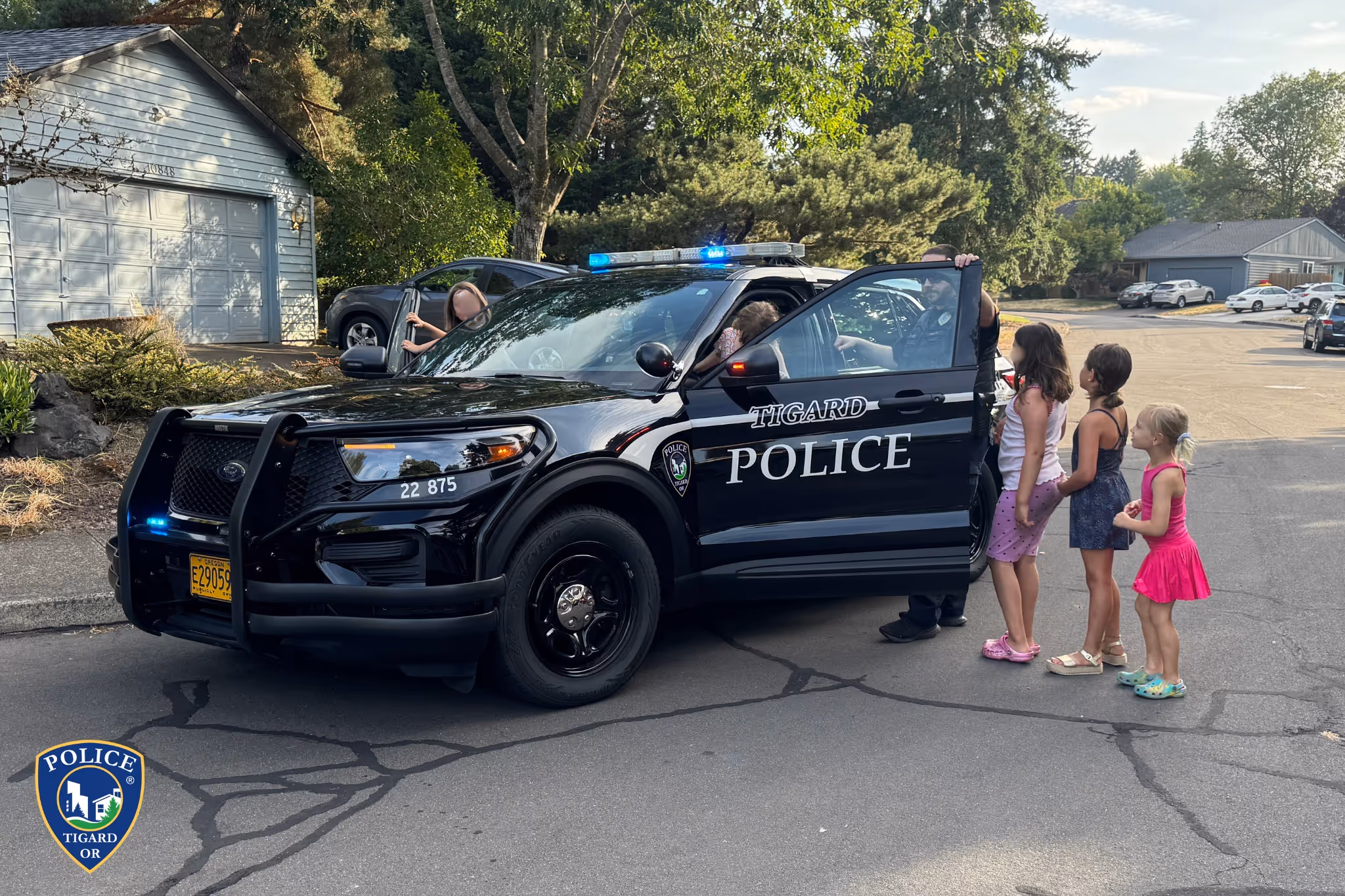 Tigard police officer showing children inside a black police SUV on a suburban street.
