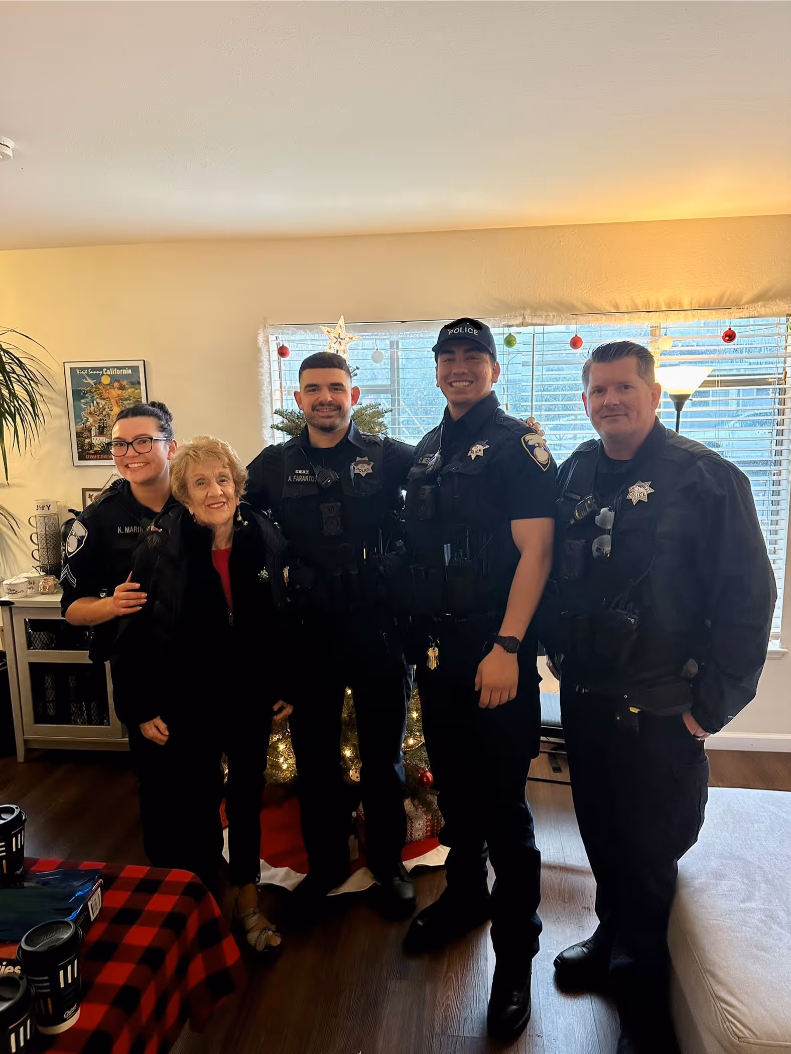Four police officers standing indoors with an elderly woman in front of a decorated Christmas tree.