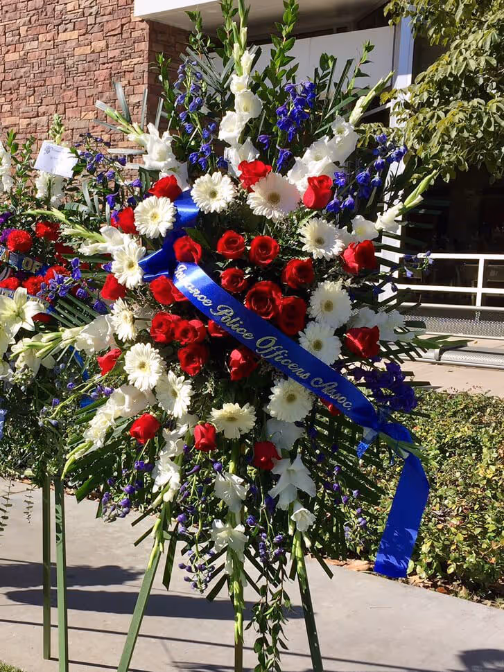 Memorial floral arrangement featuring red roses, white daisies, and purple flowers with a blue ribbon reading 'Glendale Police Officers Assoc.'