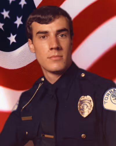 Portrait of a young male police officer in uniform with an American flag background.