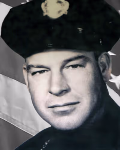 Black and white portrait of a uniformed police officer wearing a cap with a badge, with an American flag in the background.
