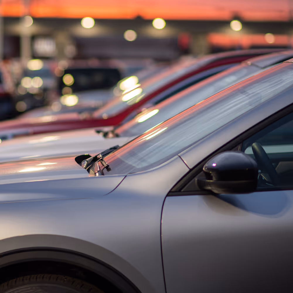 Close-up of silver car's front side parked among other cars in a lot at sunset.