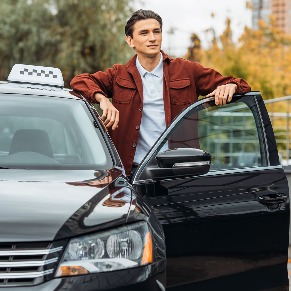 Man in red jacket standing next to an open door of a black taxi outside.