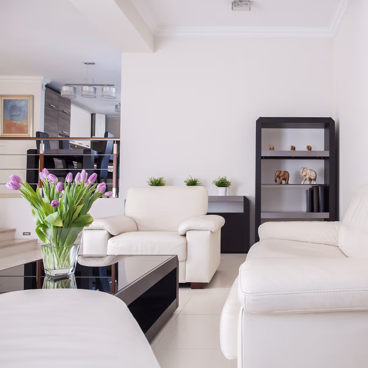 Modern living room with white leather sofas, black coffee table, and purple tulips in a glass vase.