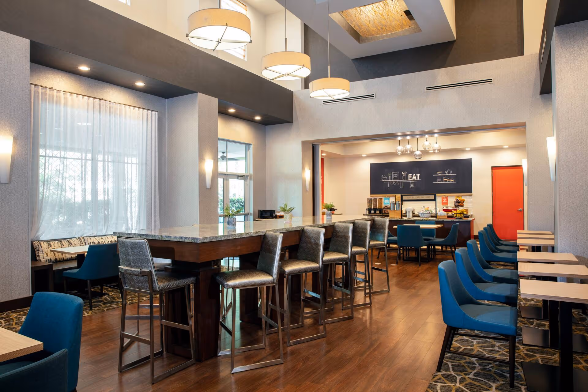 Modern cafe interior with wooden bar counter, blue seating, pendant lights, and kitchen area.