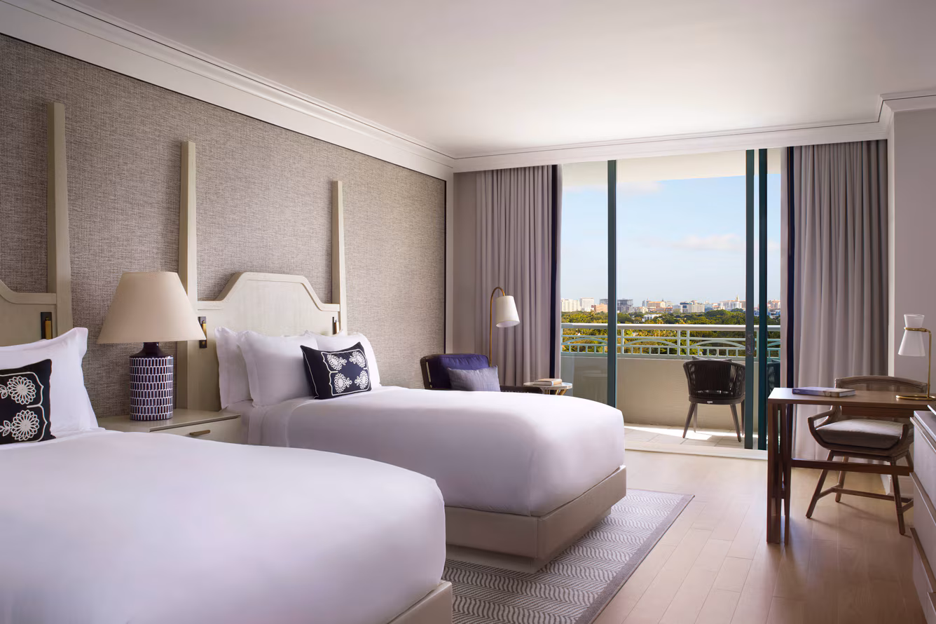 Modern hotel bedroom with two beds, city skyline view from balcony, contemporary furnishings