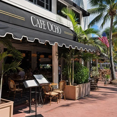 Outdoor seating area of Cafe Ocho with wicker chairs, plants, and an American flag overhead.