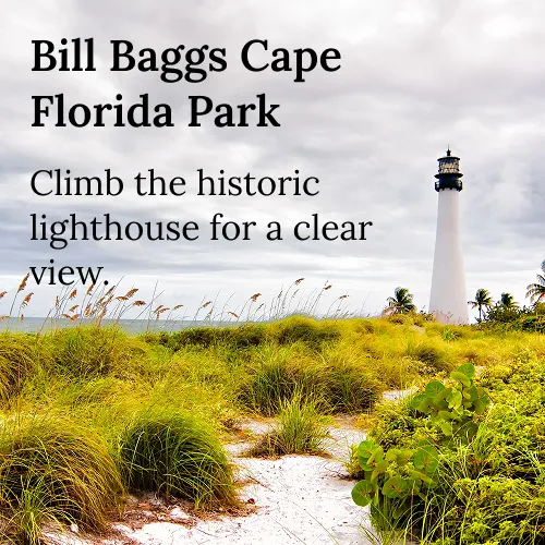 Lighthouse stands tall behind grassy sand dunes under a cloudy sky at Bill Baggs Cape Florida Park.