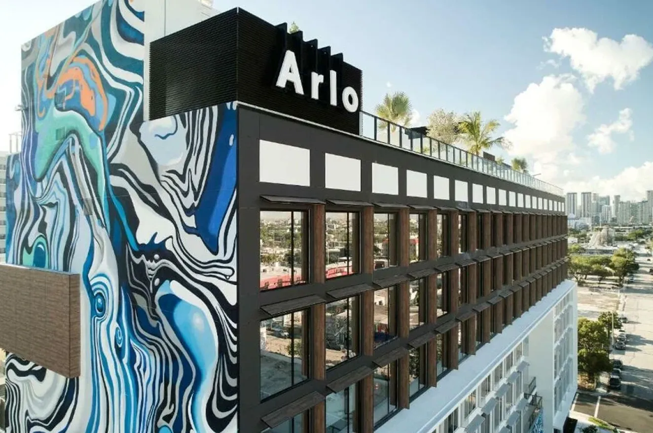 Modern building with Arlo sign and colorful abstract mural on side wall in urban area.