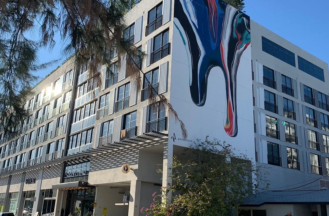 Modern multi-story building with a large colorful abstract mural on the corner wall under a clear sky.