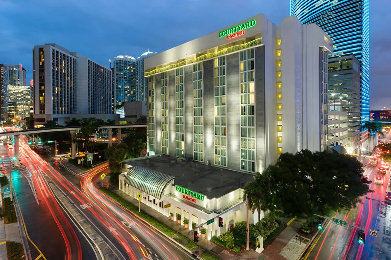 Night view of Courtyard Marriott hotel in a city with light trails from passing vehicles.