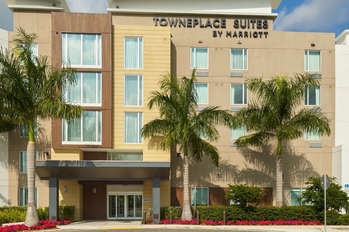 Front view of TownePlace Suites by Marriott hotel with palm trees and flower beds in front.