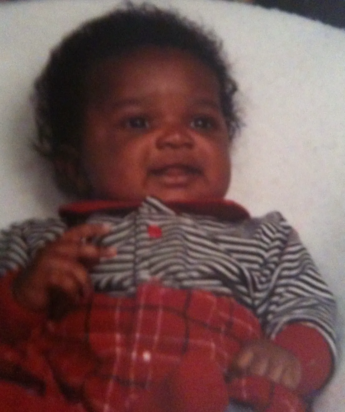 Baby wearing striped shirt with red trim looking at camera