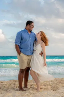 Couple standing together on beach looking at ocean waves and cloudy sky