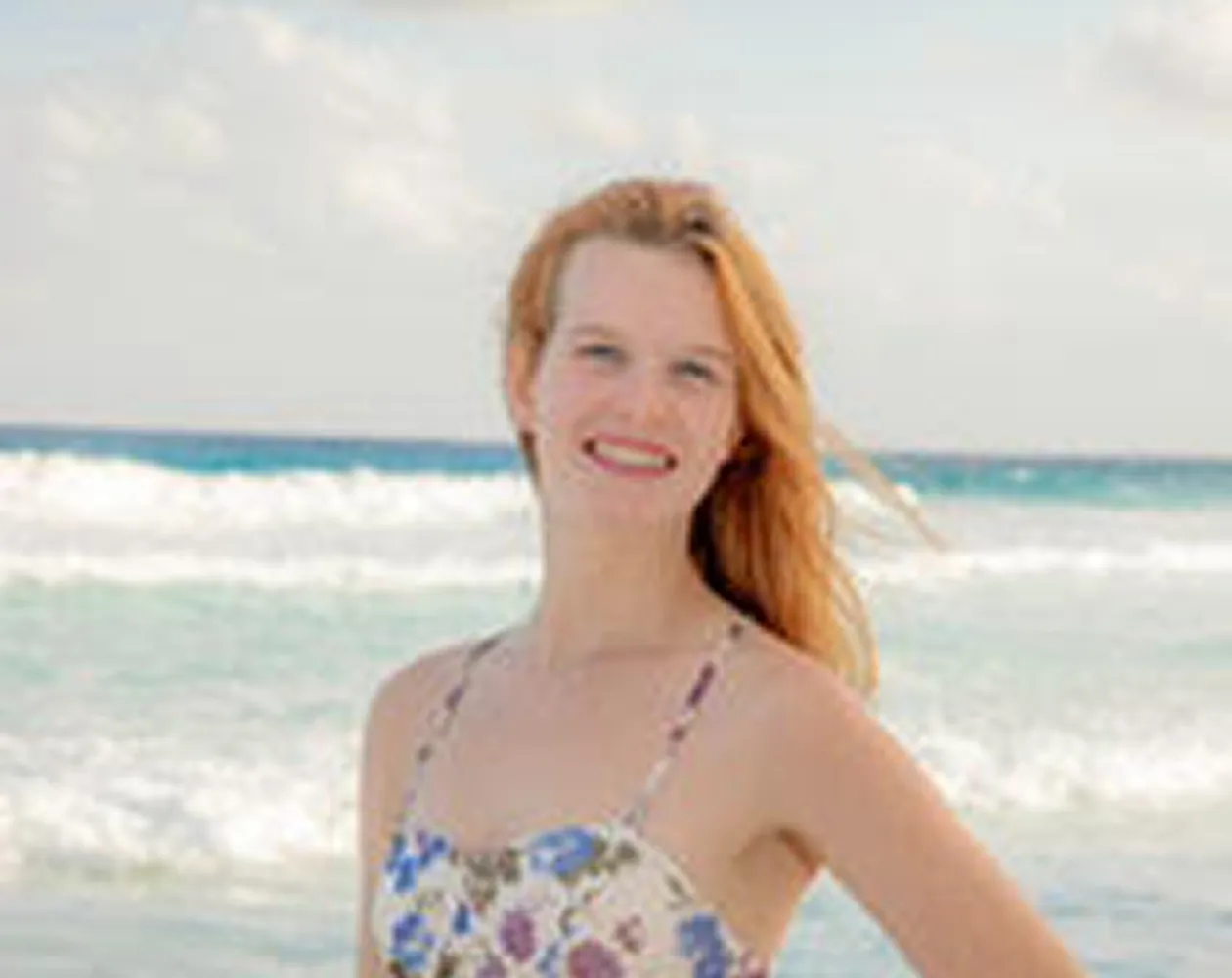 Woman with red hair smiling at beach with ocean waves behind her