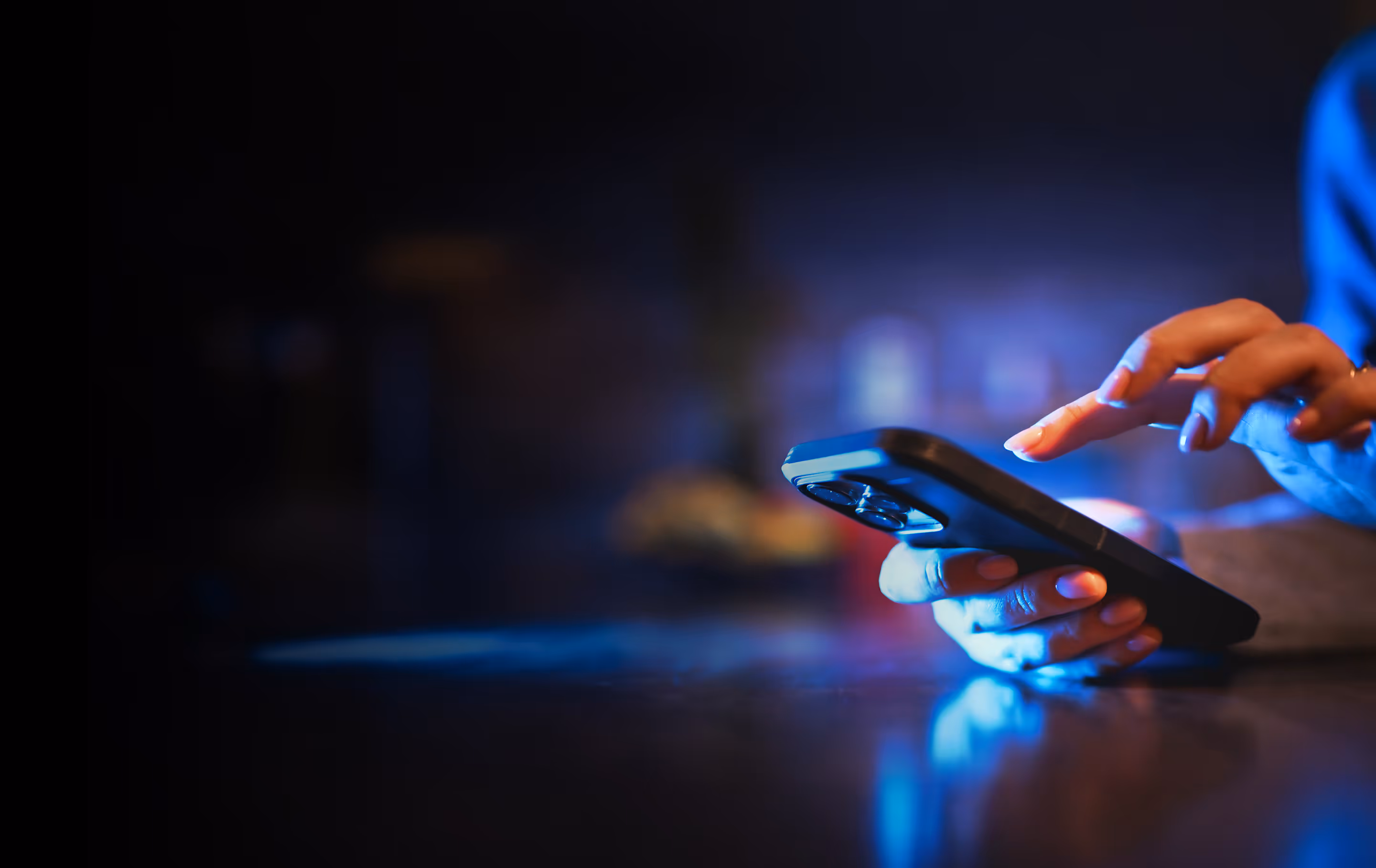 Close-up of a person’s hands using a smartphone with a dark background and blue lighting.