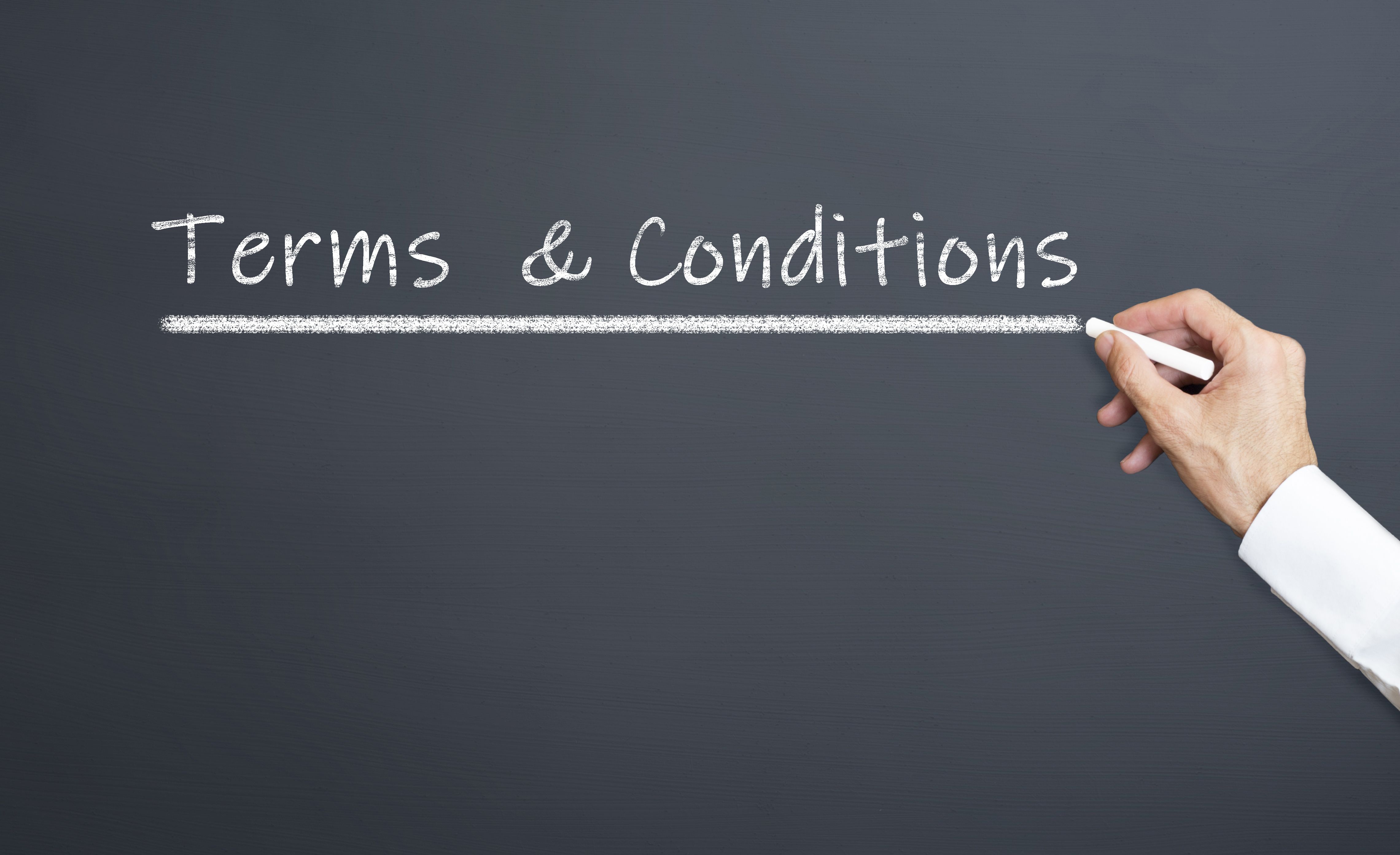 Hand writing "Terms & Conditions" underlined on a dark chalkboard with white chalk.