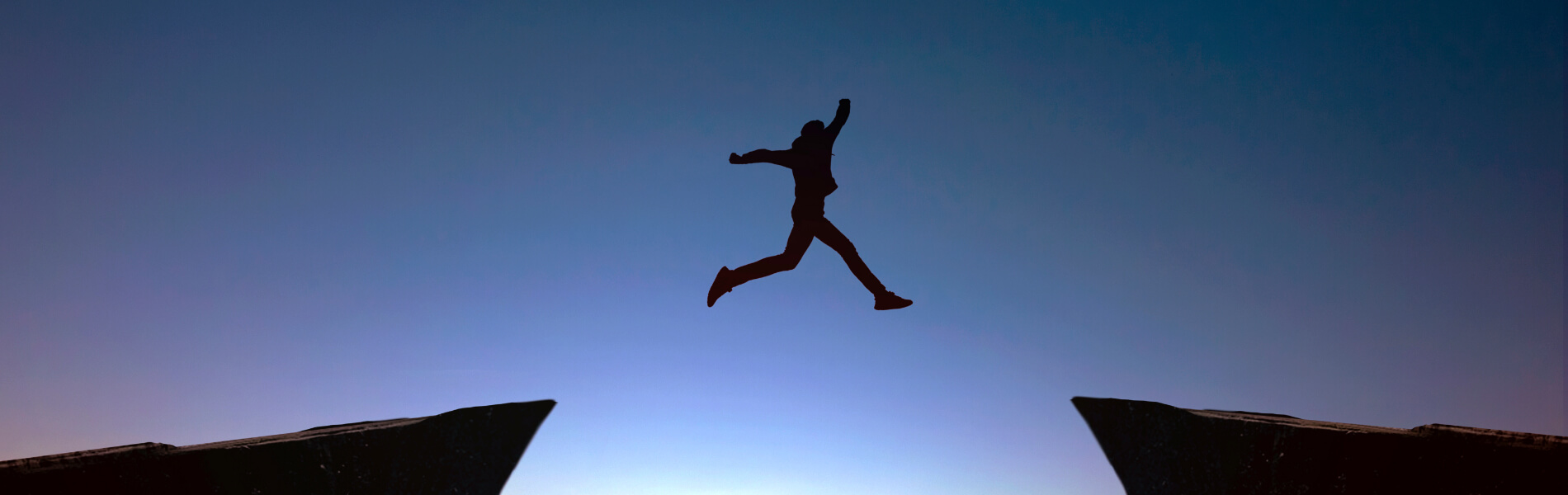 Silhouette einer Person, die nachts über eine Lücke zwischen zwei Felsen springt.