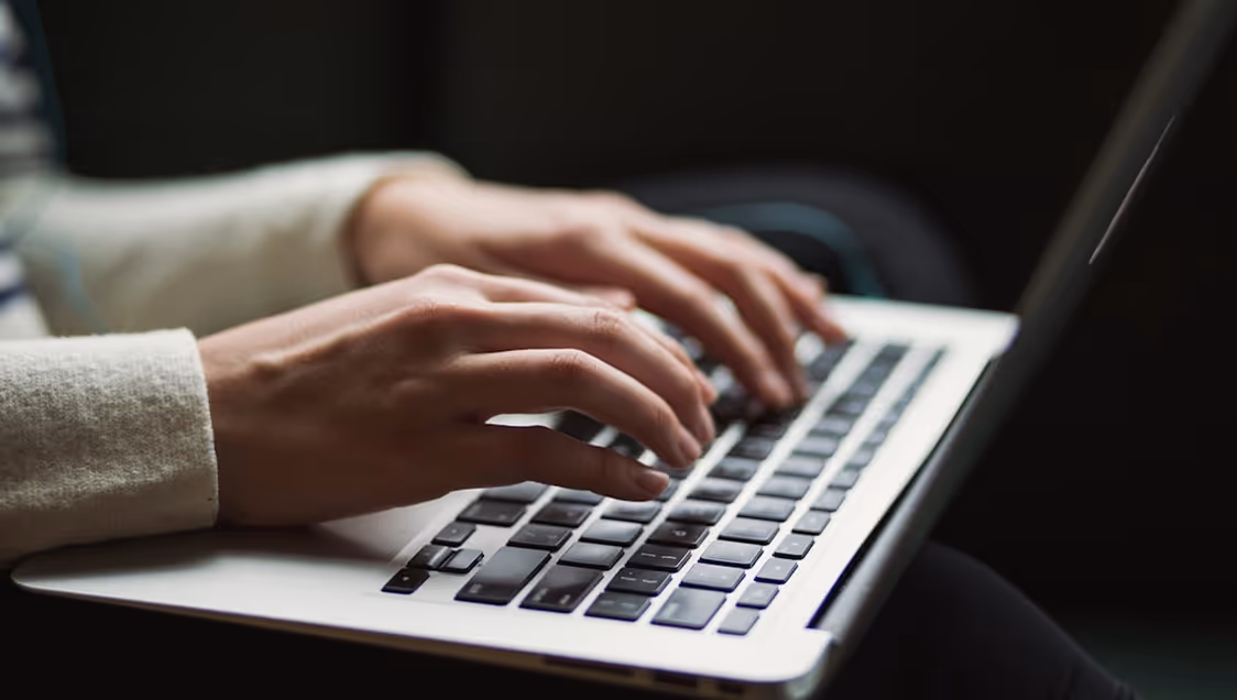 Hands typing on a laptop keyboard with a dark blurred background.