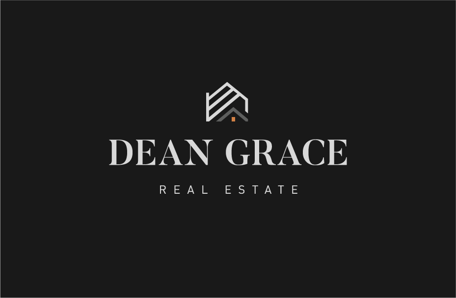 Modern living room with vaulted ceiling, black tiled fireplace with mounted TV, gray armchairs, glass coffee table, and large windows showing trees outside.