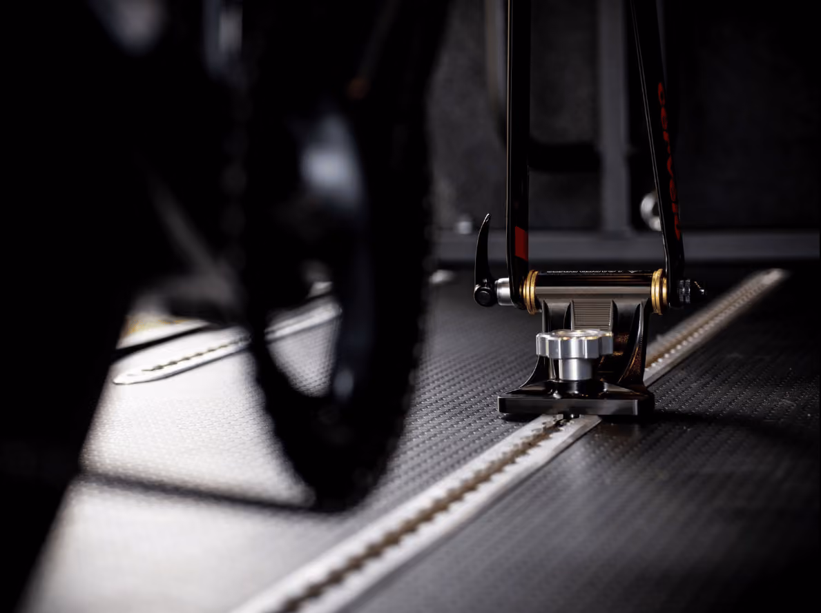 Close-up of a bike frame secured on a bike trainer or repair stand on a textured floor.