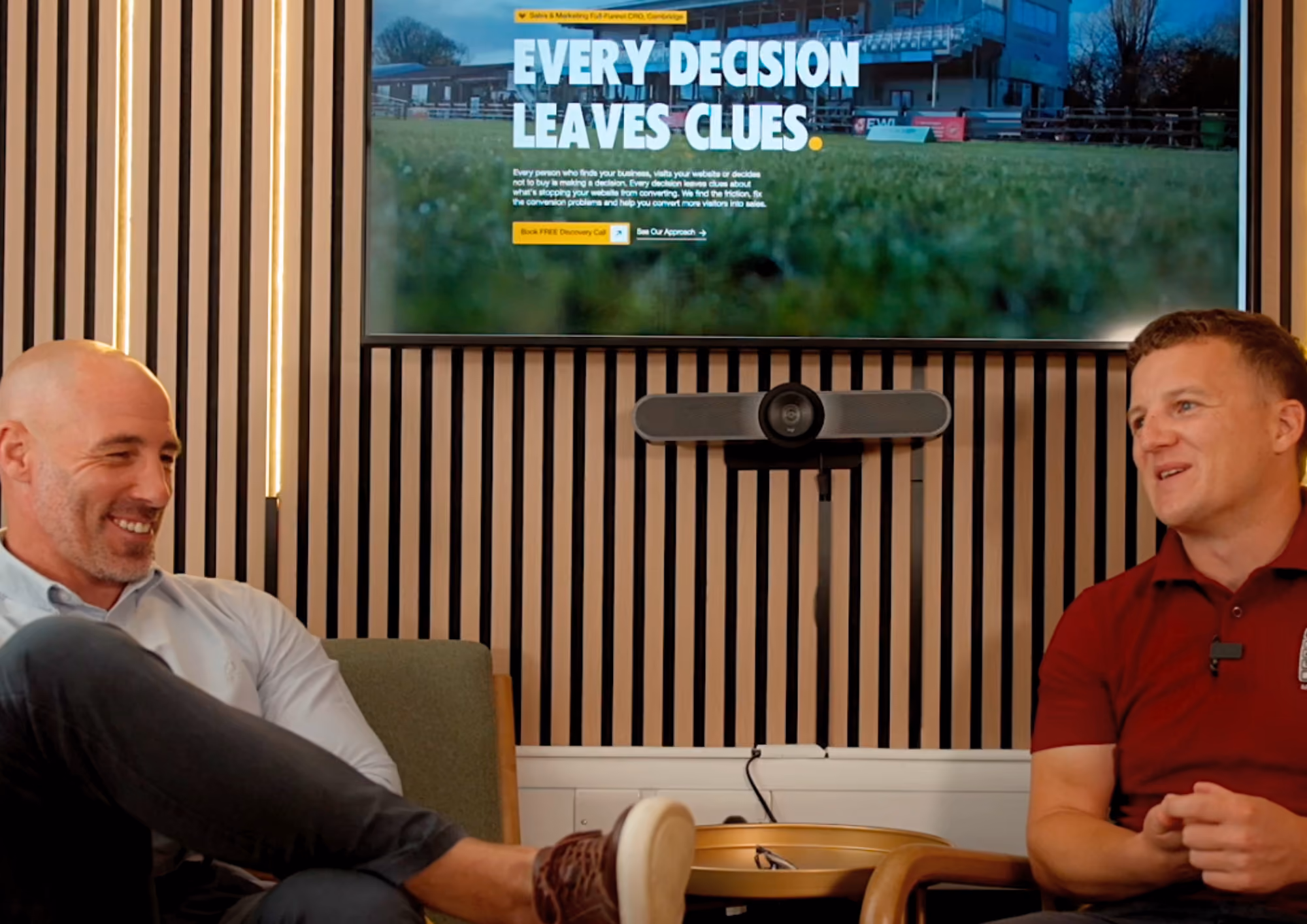 Two men seated and talking in front of a screen displaying 'Every decision leaves clues' text.