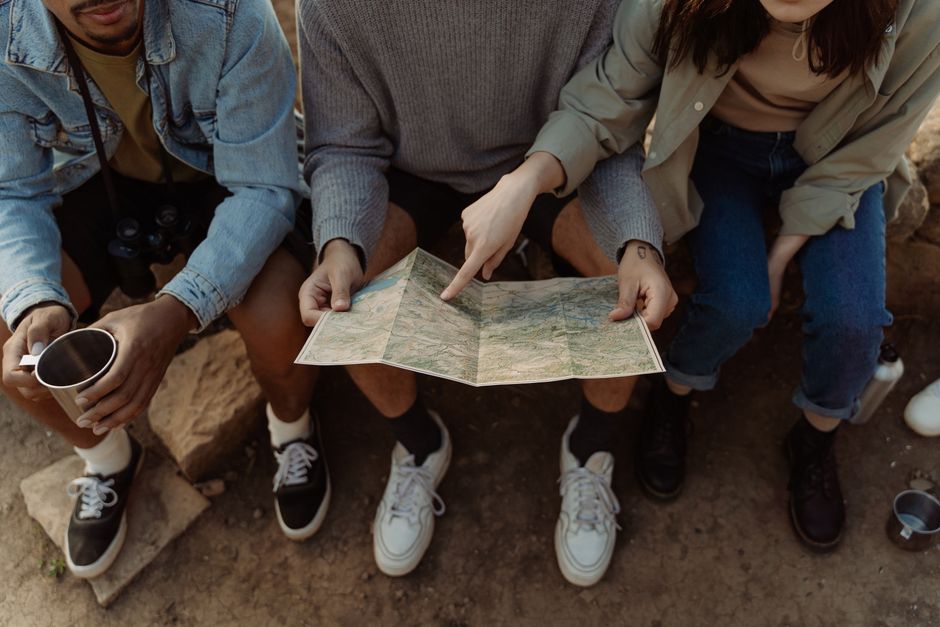 Group of friends sitting together, exploring a map for their next adventure, creating exciting travel plans.