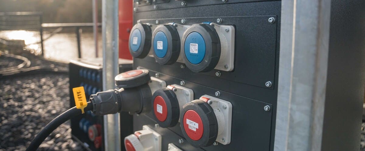 Close-up of a black electrical panel with multiple industrial blue and red power sockets, one connected to a large black cable.