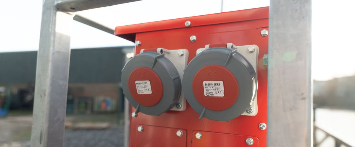 Close-up of two industrial Mennekes electrical sockets mounted on a red metal panel outdoors.