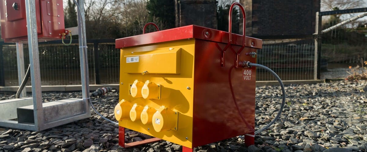 Red and yellow portable electrical transformer box labeled 400 volt on gravel ground outdoors.