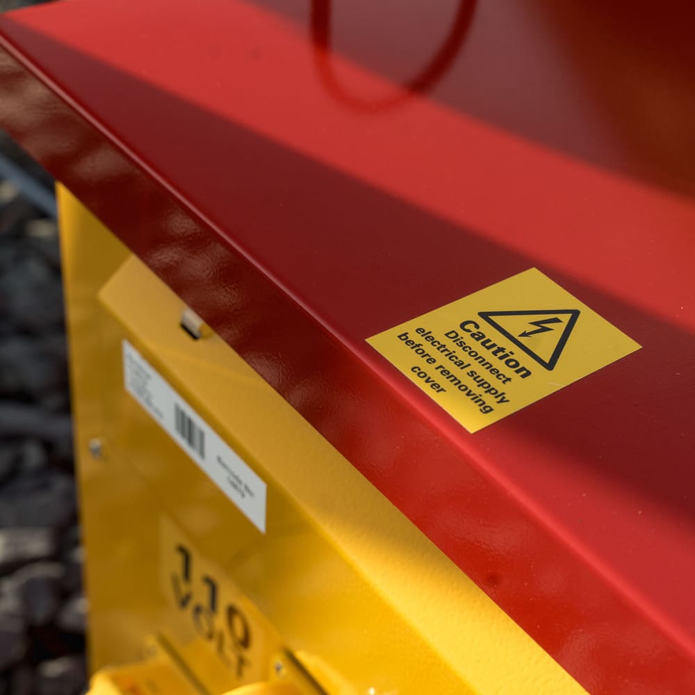 Close-up of a red and yellow electrical device with a caution sticker warning to disconnect electrical supply before removing the cover.