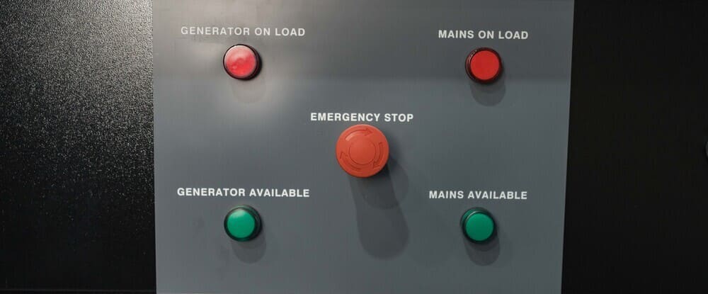 Control panel with five indicator lights and an emergency stop button labeled for generator and mains power status.