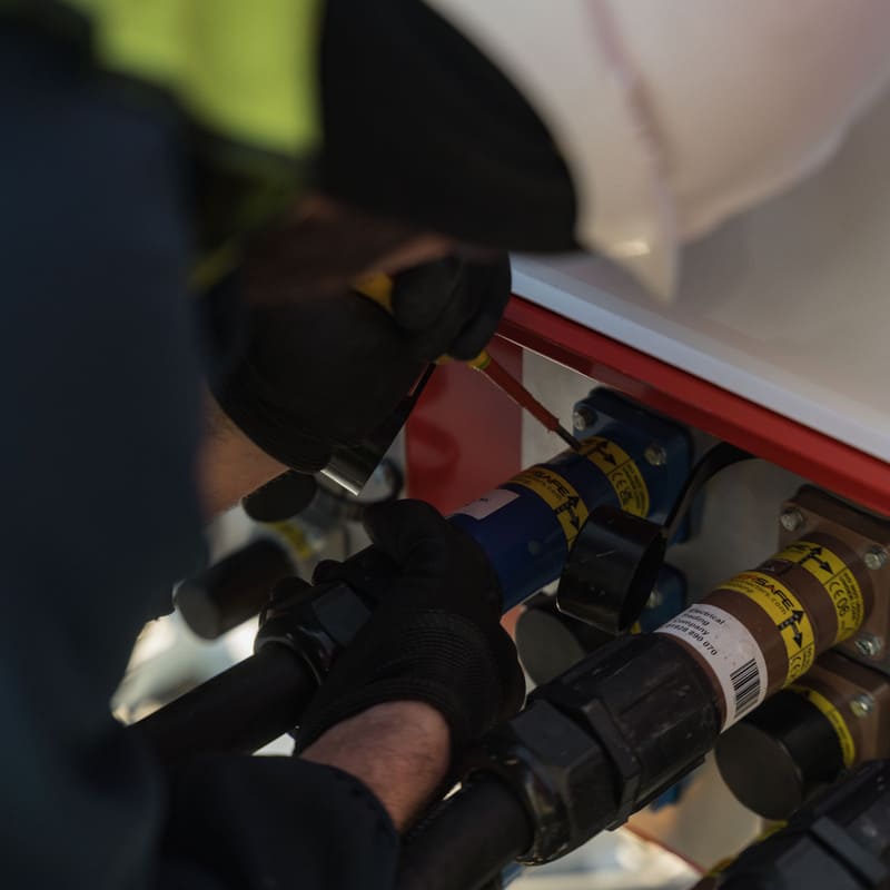 Worker in safety gear using a screwdriver to adjust electrical connectors on equipment.