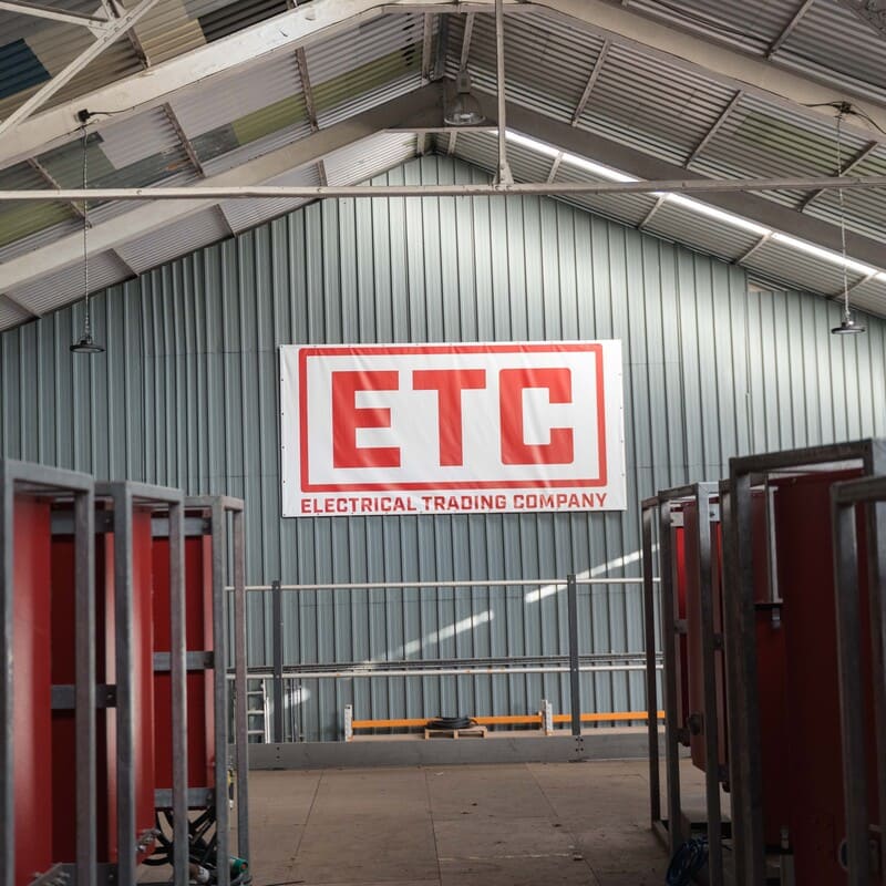 Large indoor warehouse space with a corrugated metal wall displaying a white banner with red letters reading 'ETC Electrical Trading Company.'