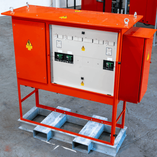 Orange industrial electrical control panel mounted on a metal frame in a workshop.