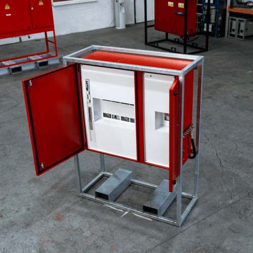 Red metal electrical panel with an open door showing circuit breakers inside, mounted on a metal frame in an industrial setting.