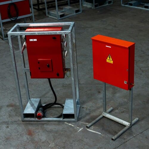 Two industrial red metal electrical control boxes mounted on metal stands on a concrete floor.