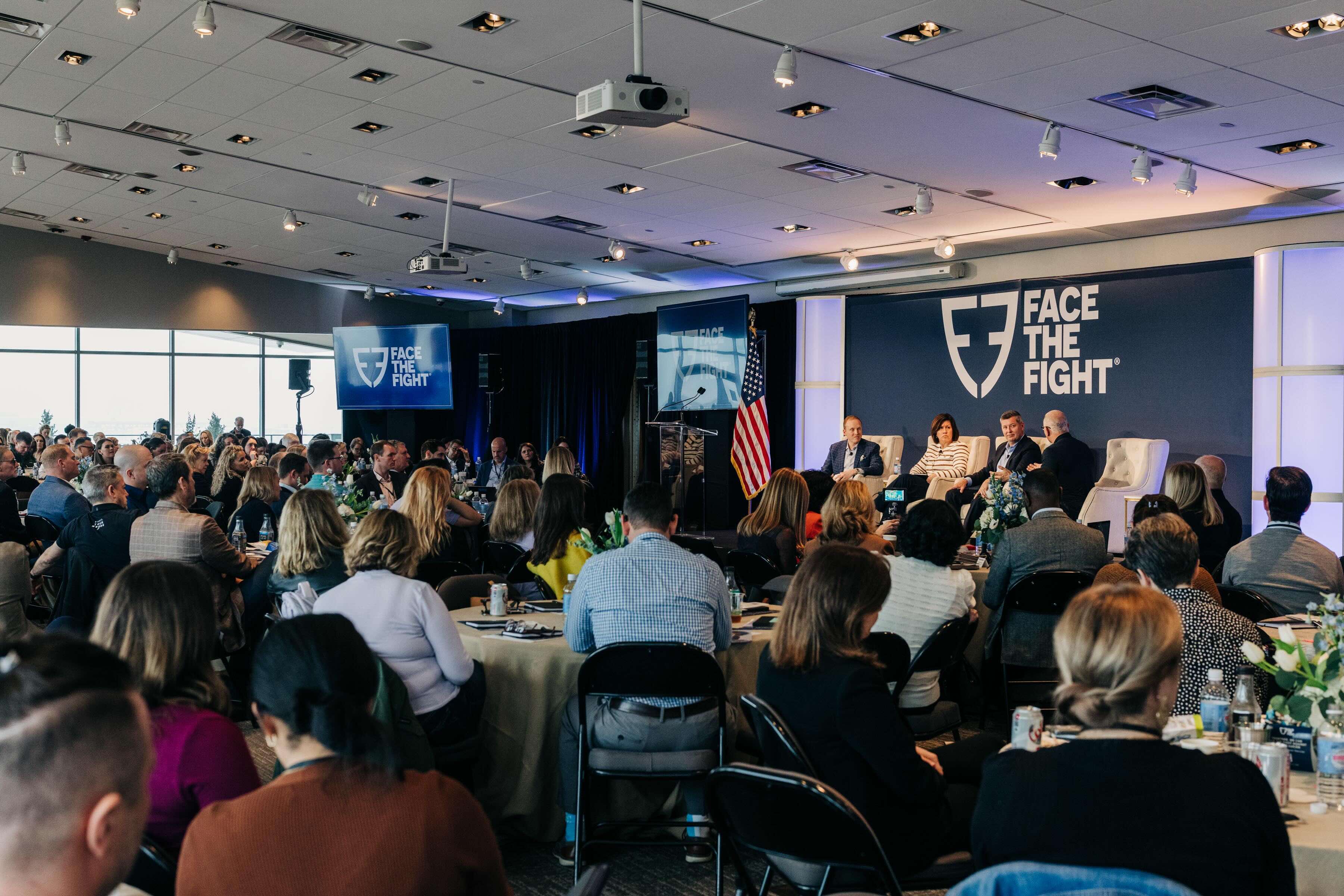 Audience seated at round tables listening to a panel discussion on stage with 'Face The Fight' logo displayed behind them at the 2026 Annual Coalition Convening.
