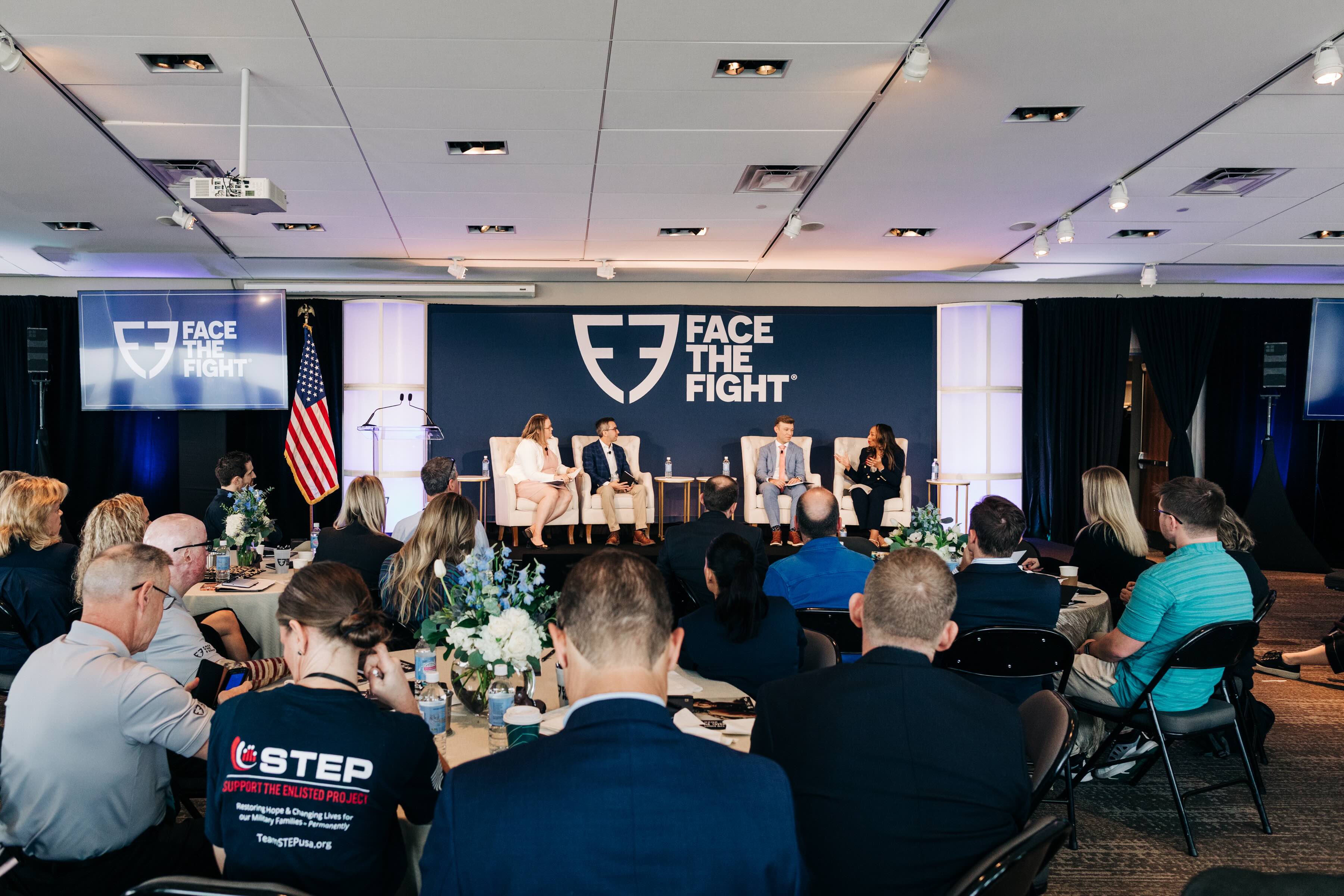 Audience seated at round tables watching a panel discussion with four speakers on a stage with Face The Fight logos and an American flag.