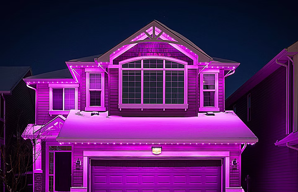 Two-story house illuminated with bright purple outdoor lighting against a dark night sky.