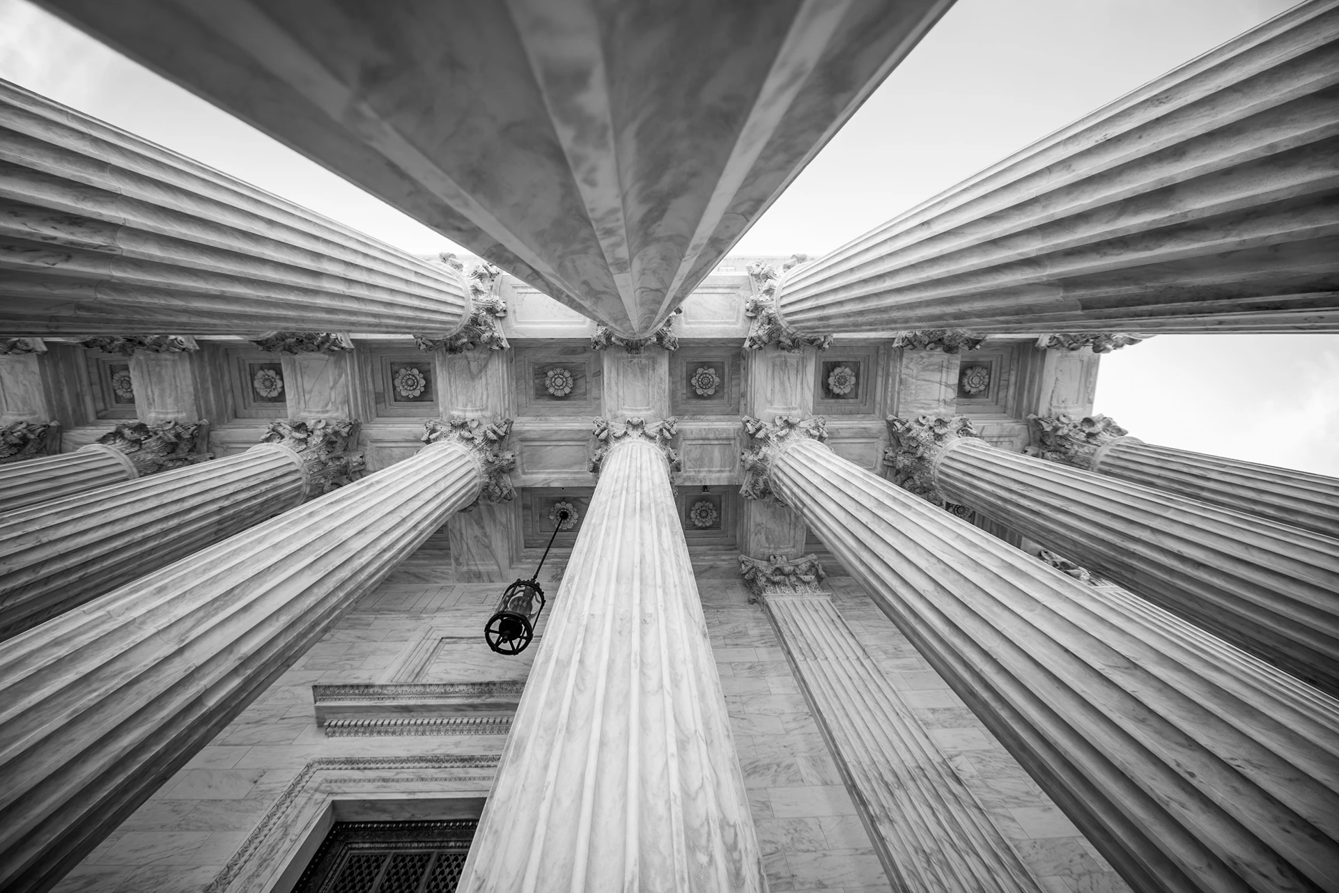 Low-angle black and white photo of tall classical columns with ornate capitals supporting a building ceiling.