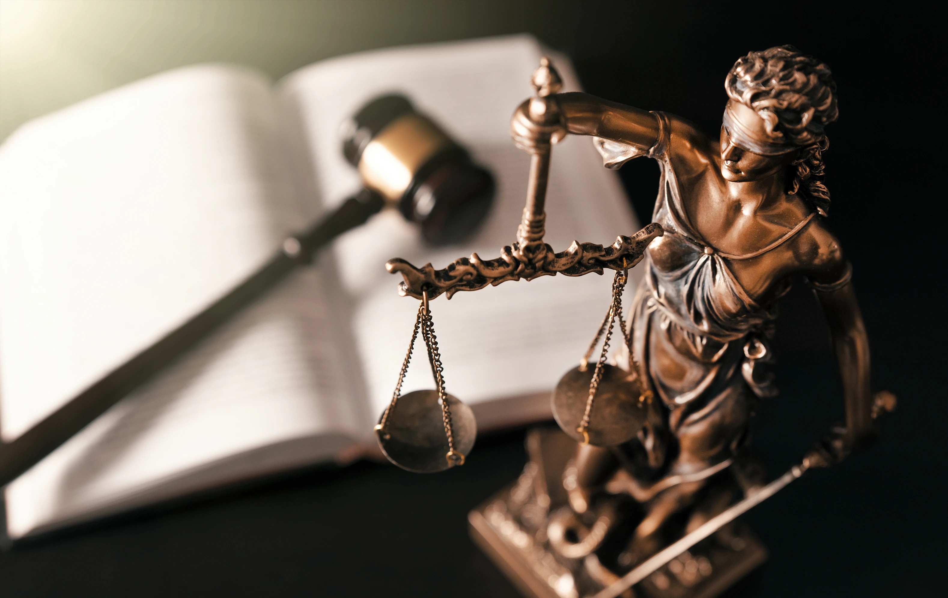 Bronze statue of Lady Justice holding scales and sword with a gavel and open law book blurred in the background.