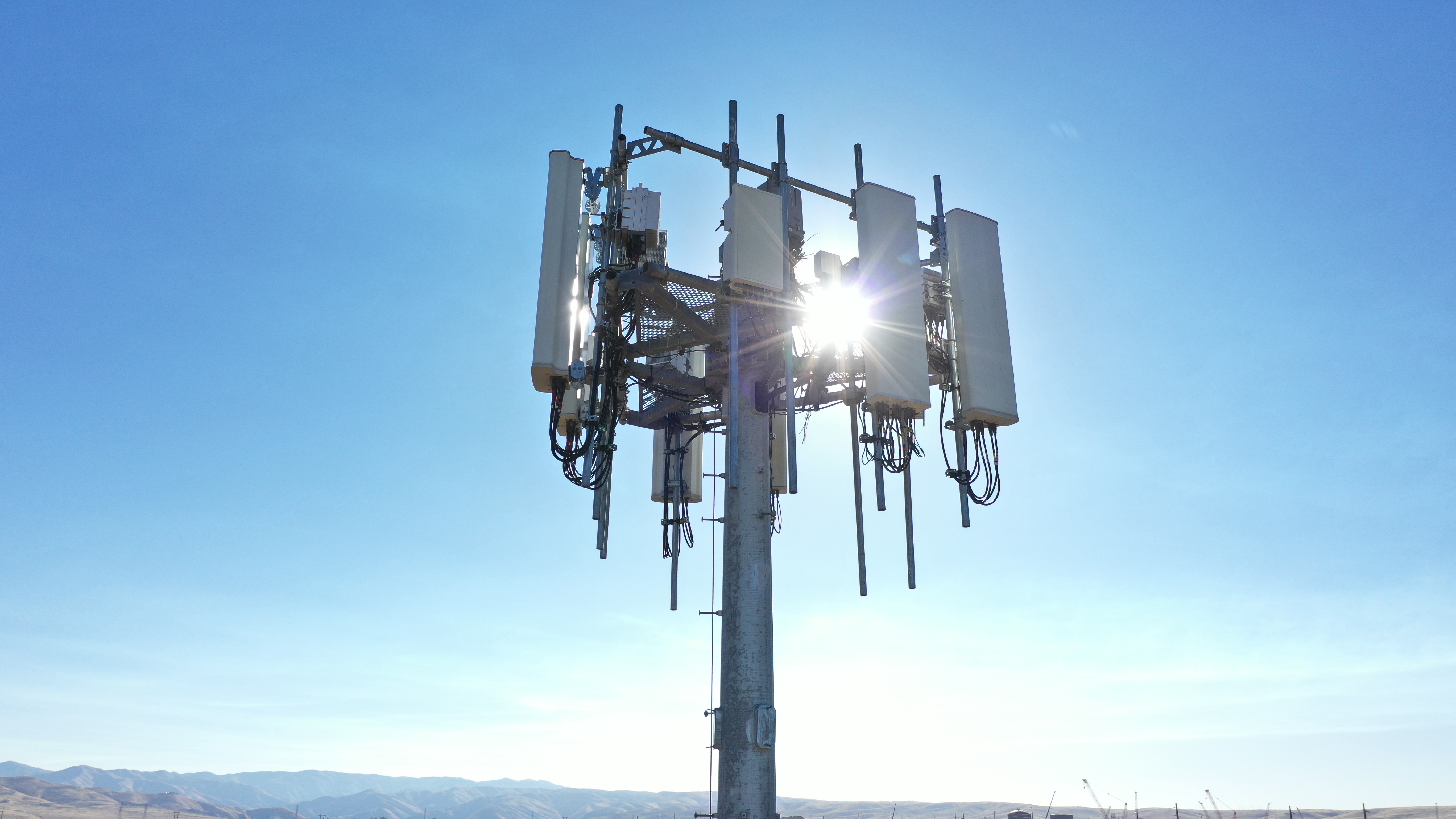 Cellular tower with antennas under clear blue sky and mountains in the background.