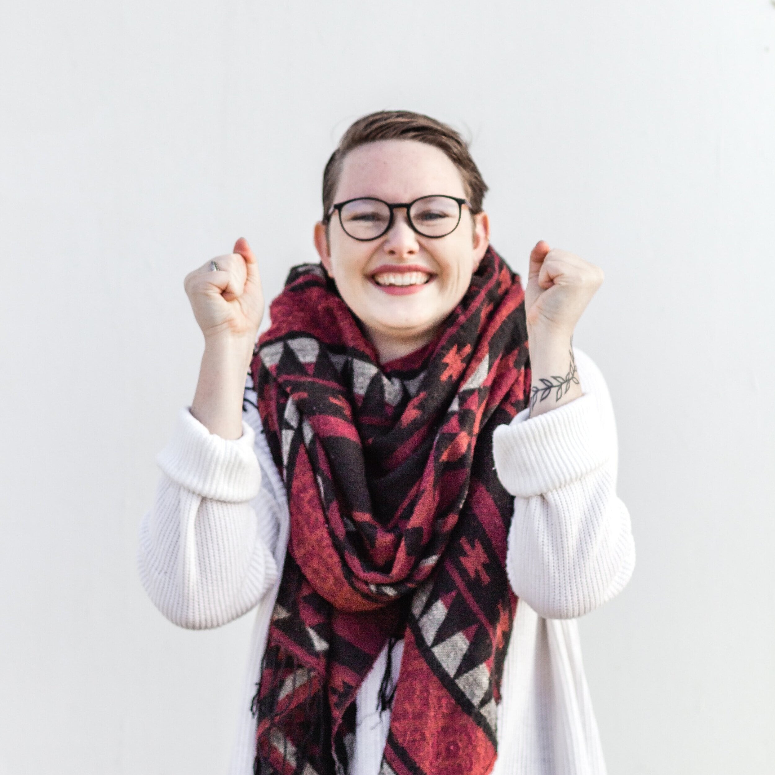 A woman posing for the camera. She has a big smile on her face and her arms raised up excitedly in front of her body.