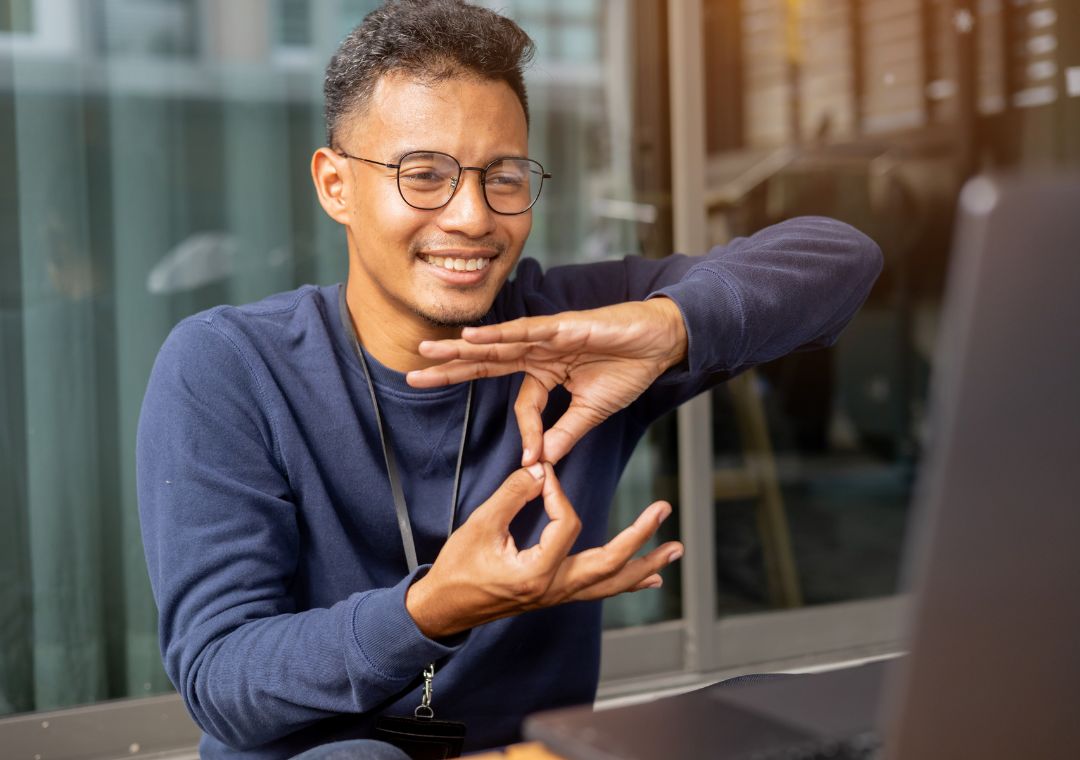 A man is using sign language to communitcate through someone via his laptop camera.
